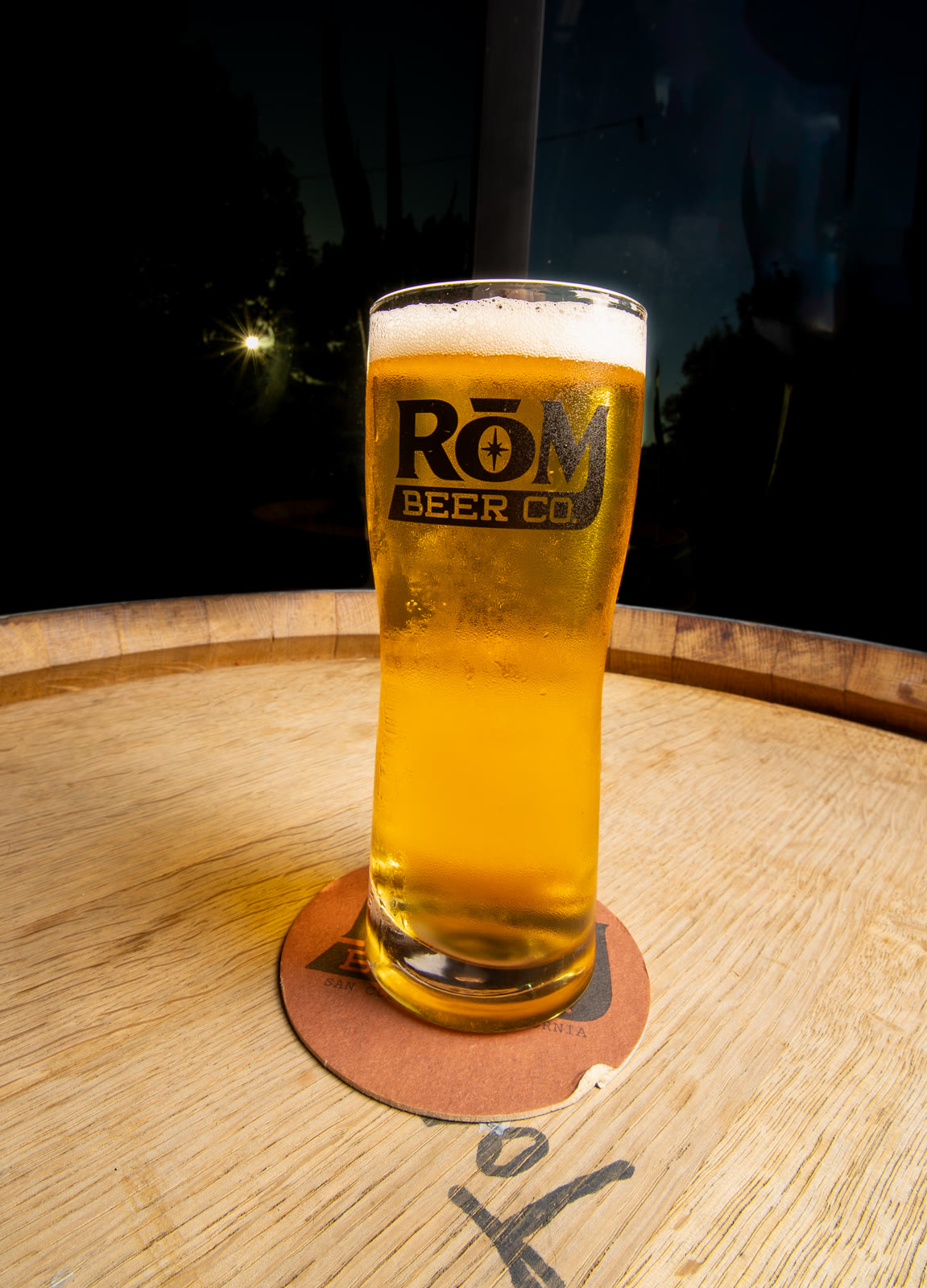 A glass of RŌM beer on a wooden table in warm light.
