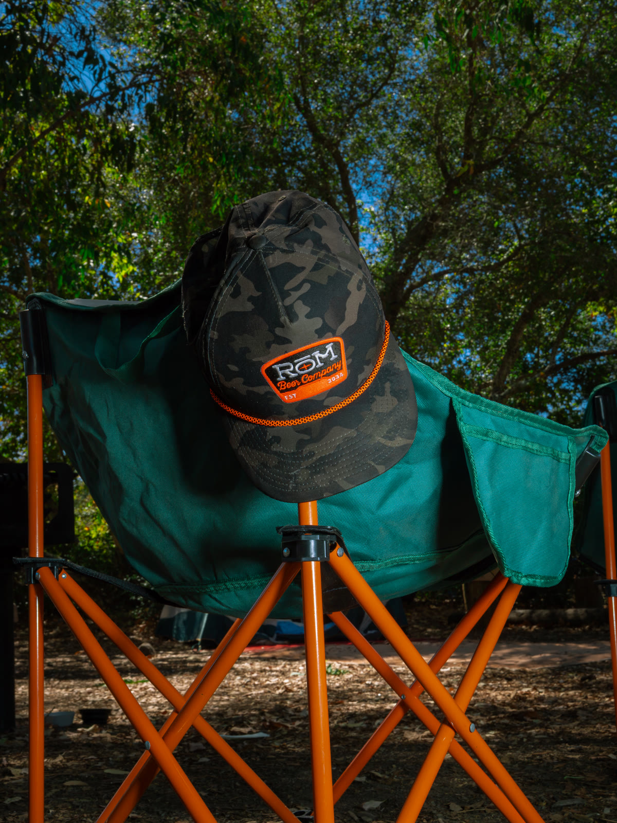 A RŌM cap resting on a camping chair outdoors.