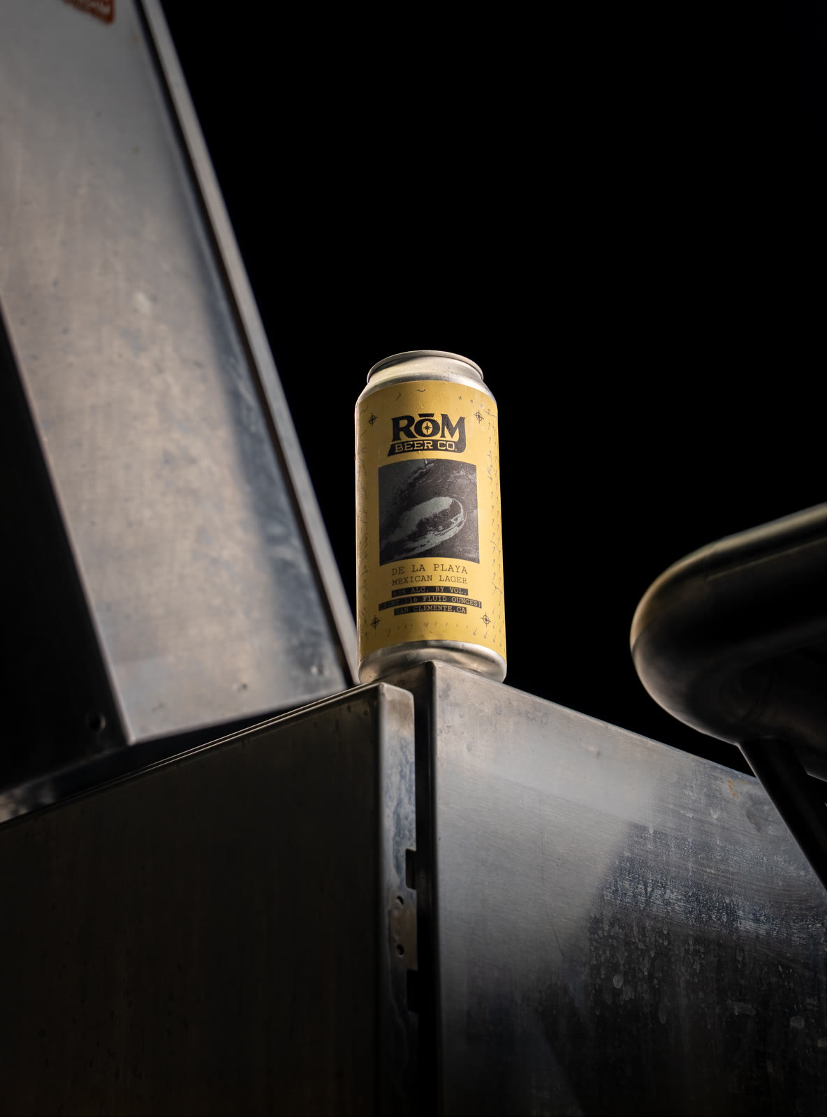 A beer can framed against dark industrial surfaces.